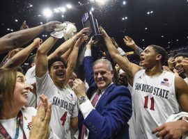 Head coach Brian Dutcher and San Diego State players hold up the Mountain West season championship trophy after defeating New Mexico. (Image: Denis Poroy/AP)